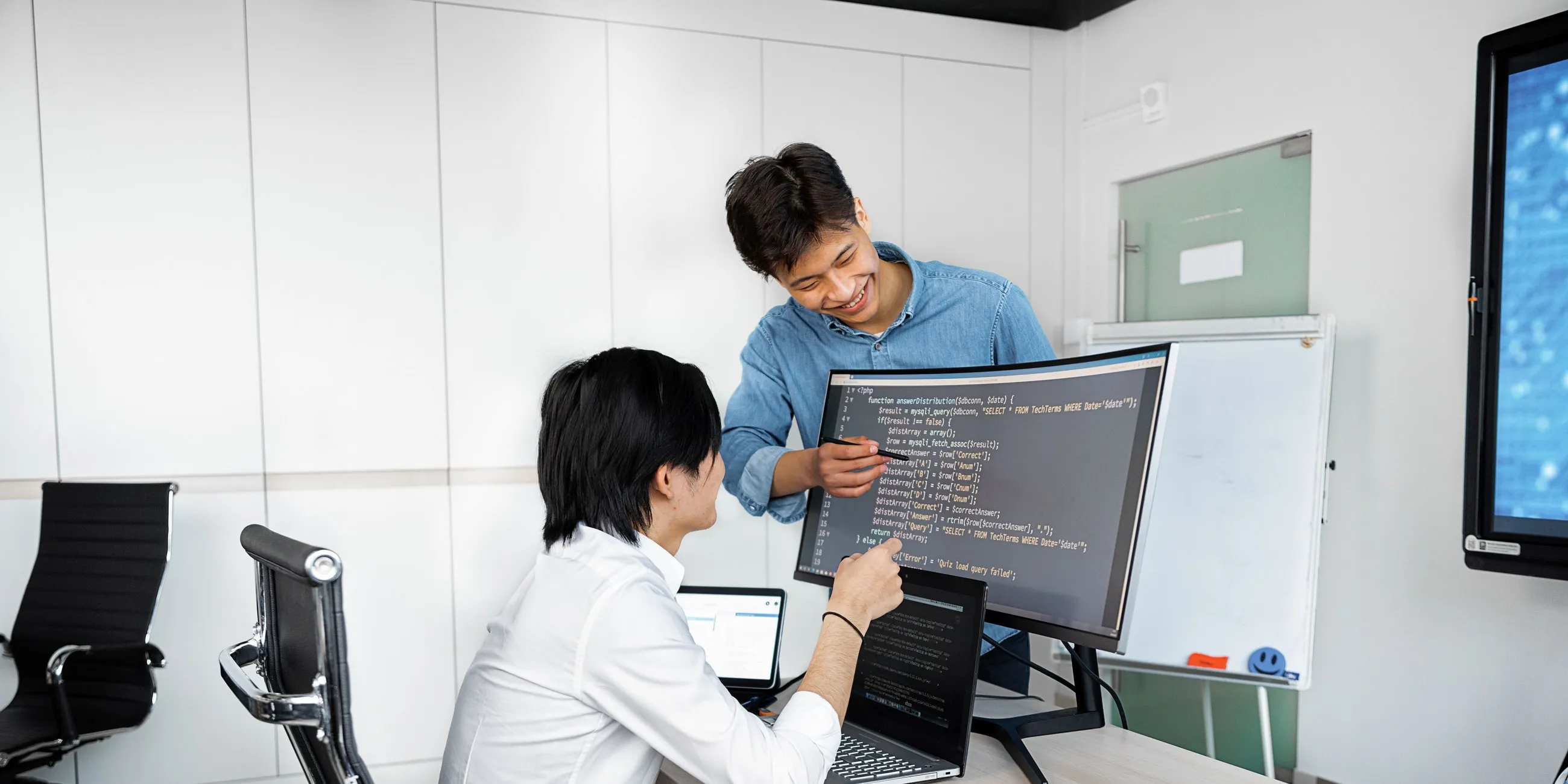 Dua developer Creative Solution Digital berdiskusi sambil meninjau kode di layar monitor